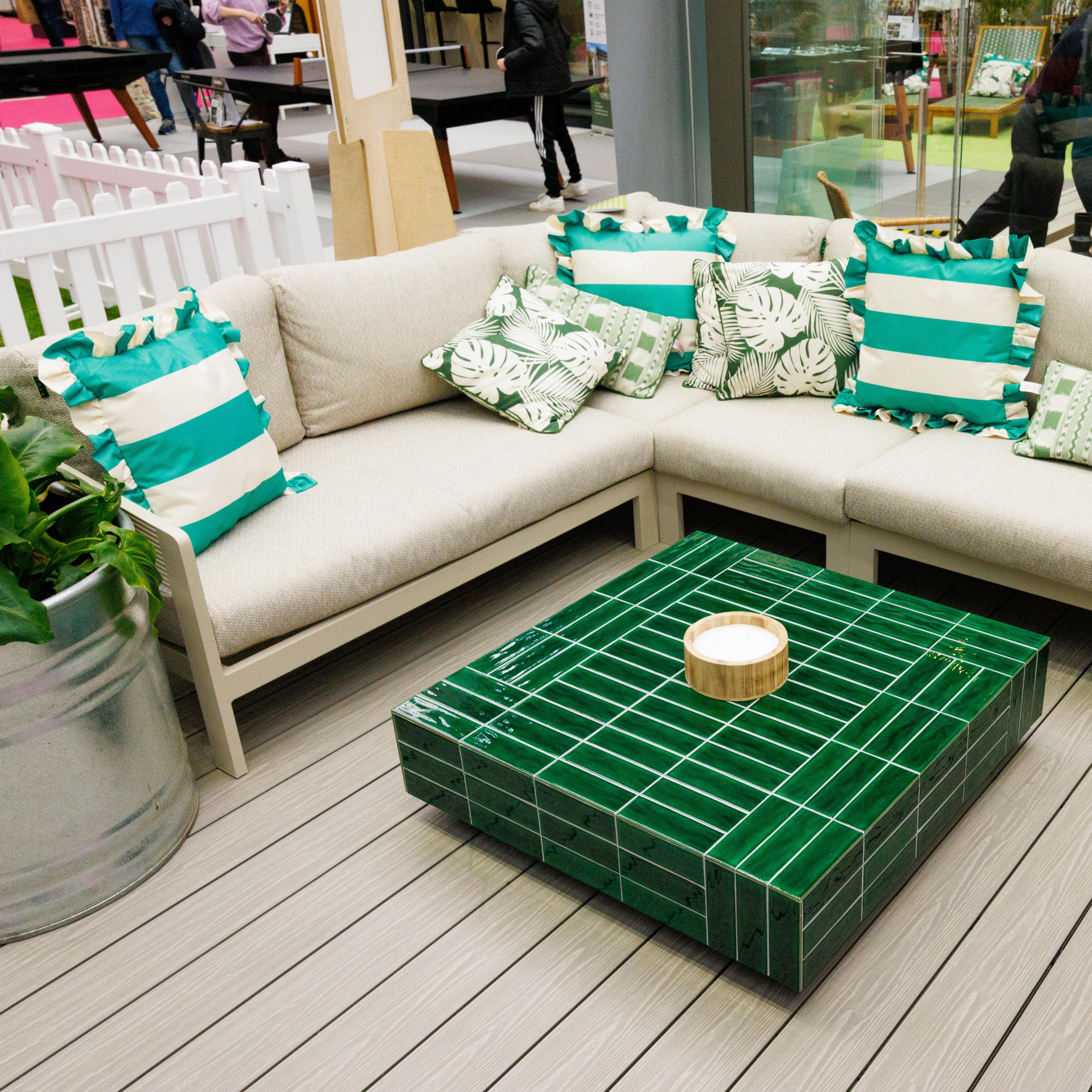 Outdoor seating area with beige sofa, green and white striped cushions and green coffee table on a light grey composite deck.