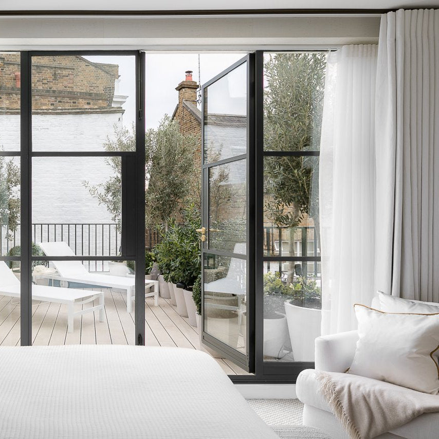Modern living room with large glass doors leading to a patio area with sun loungers on a light grey composite deck.