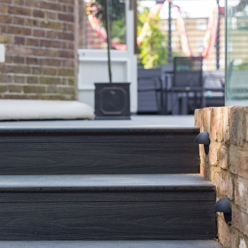 Black composite decking steps leading up to a brick building with a blurred background.