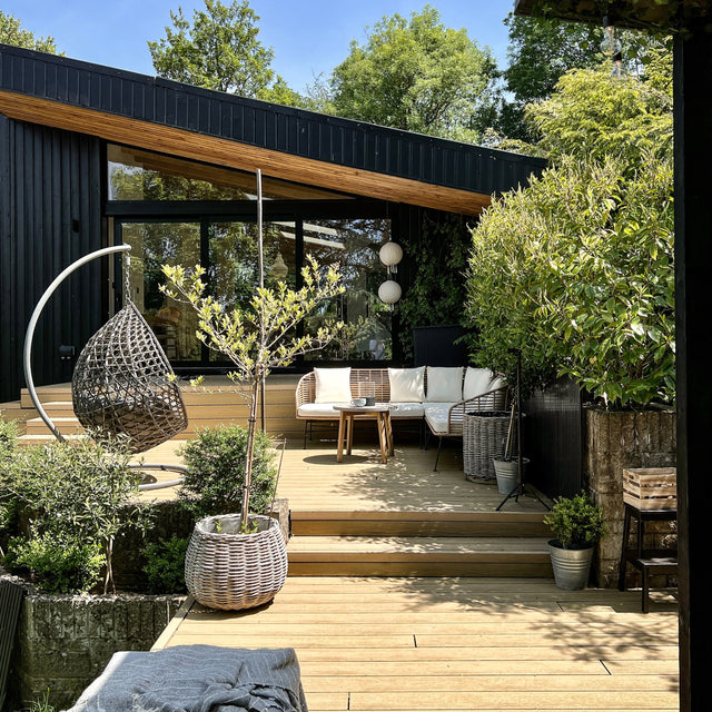 Modern outdoor composite deck patio with seating area, plants and a clear blue sky.